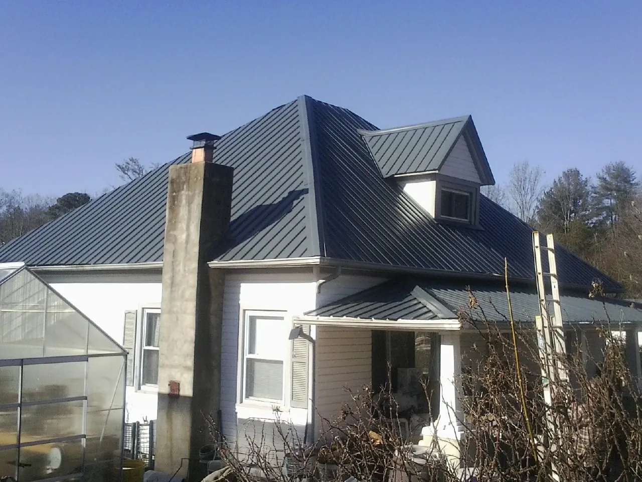 Dark blue standing seam metal roof on a white farmhouse with dormer — Slate & Tile Roof Repair by Roofing Brothers in Leonia