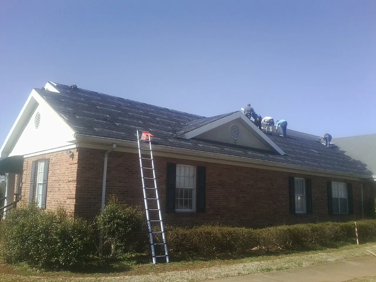 Crew tearing shingles off a brick ranch roof with a ladder set — Metal Roof Repair work by our crew in Leonia