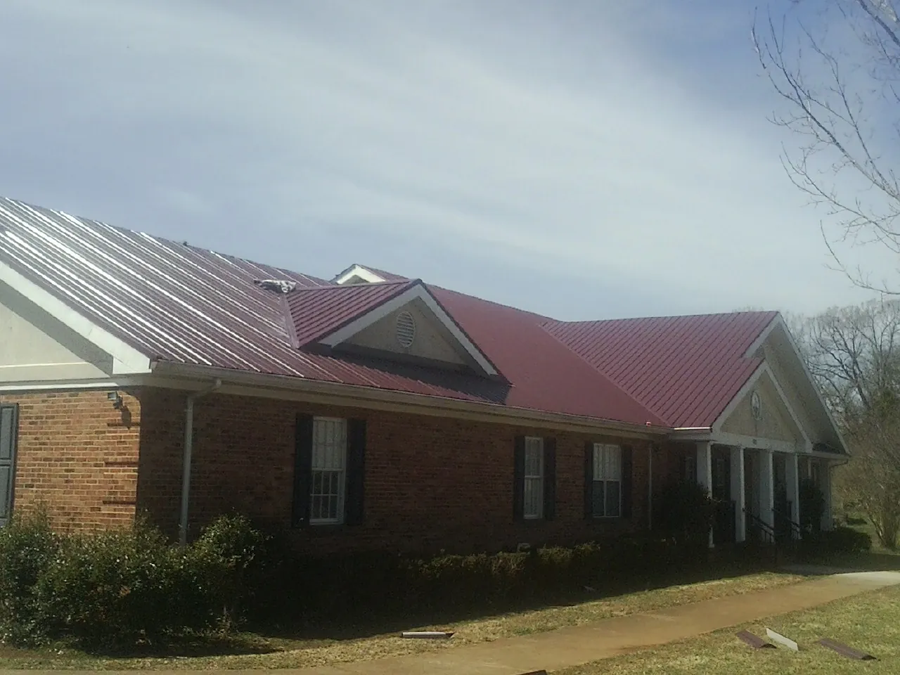 Red metal roof with gabled entries on a long brick building, from a Hail Damage Roof Repair job in Leonia