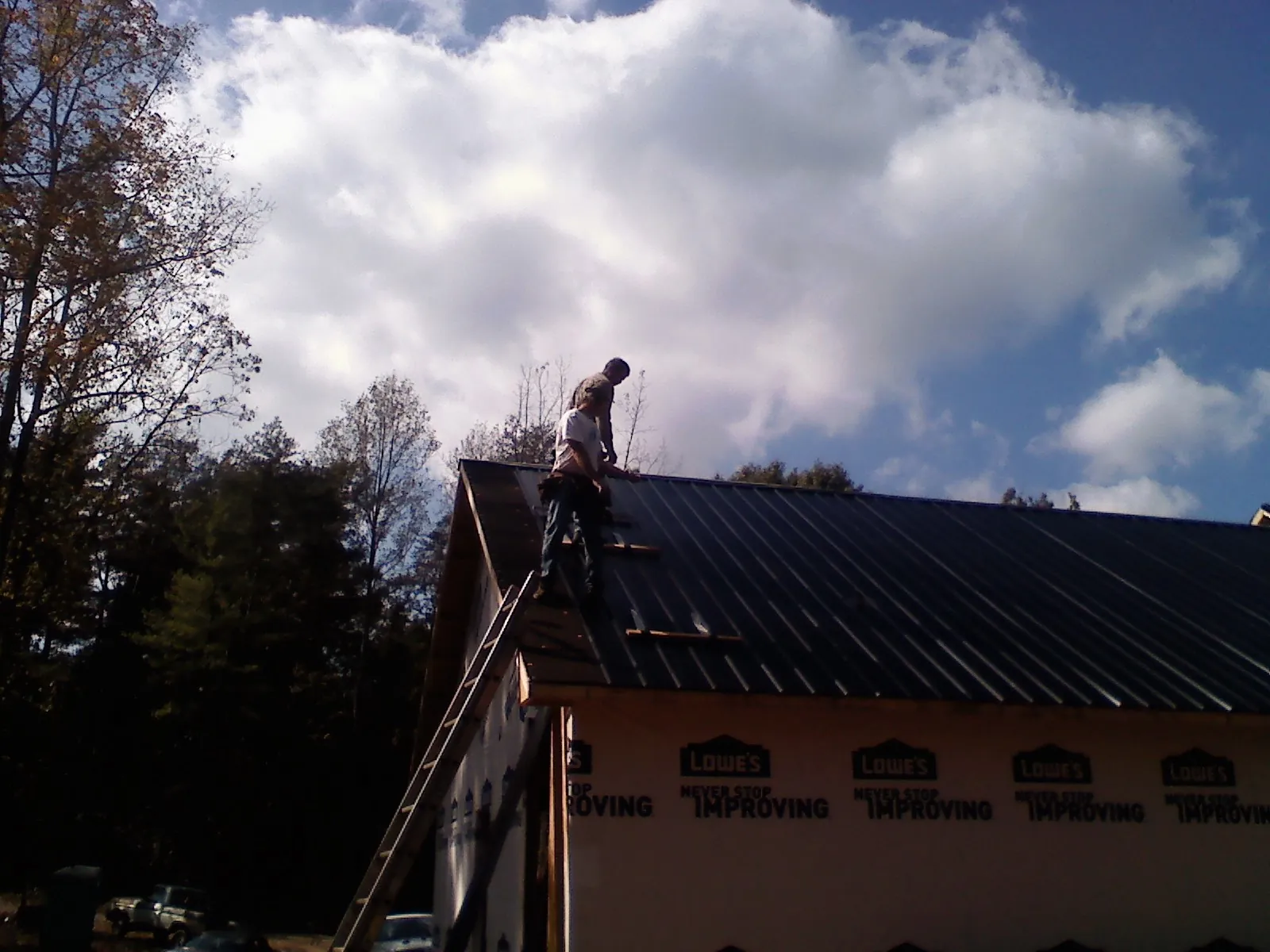 Roofer fastening dark metal panels high against a cloudy sky, from a Roof Inspection job in Leonia
