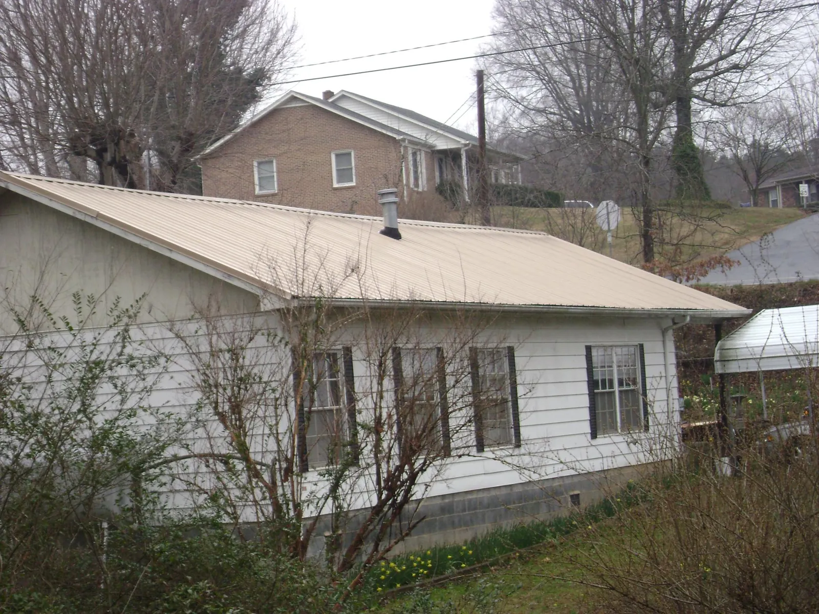 Tan metal roof on a white sided house set into a hillside — Commercial Roofing by Roofing Brothers in Leonia